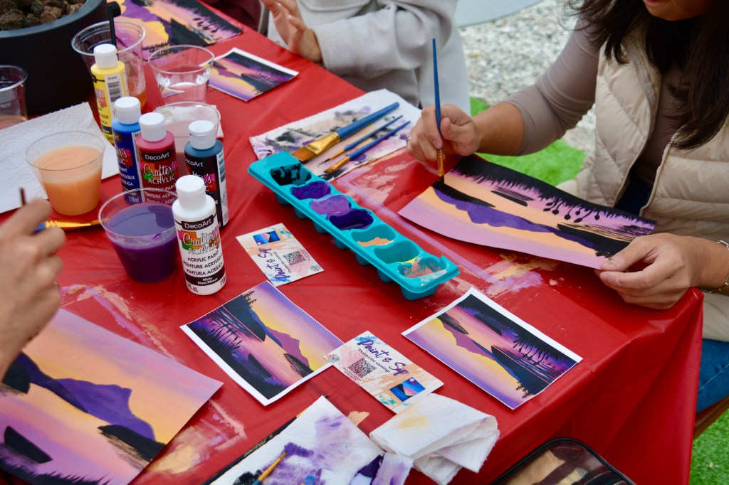 paint supplies including paint, canvas, water cup and egg carton on a red picnic table